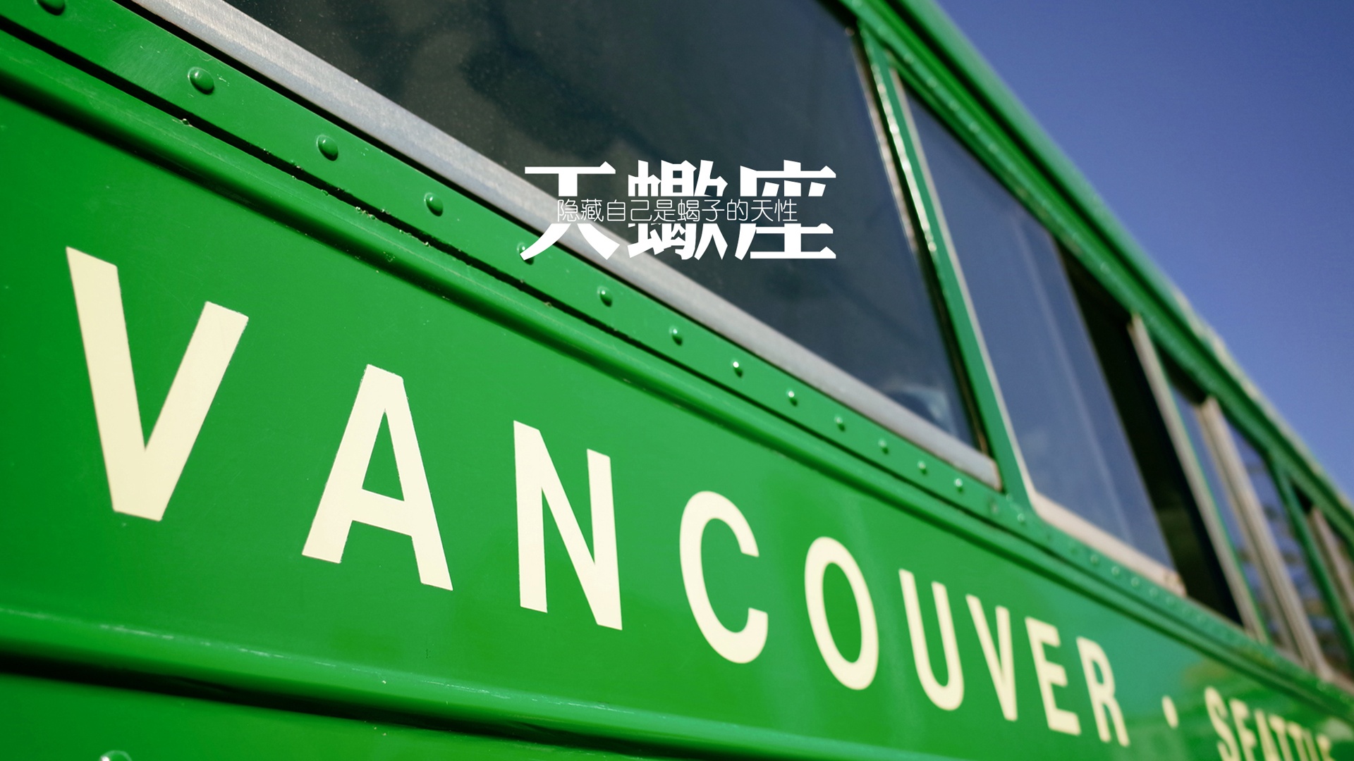 低角度拍摄的亮绿色老式巴士局部，车身上印有VANCOUVER字样，搭配纯净深蓝色天空，车窗旁有天蝎座相关白色文字。