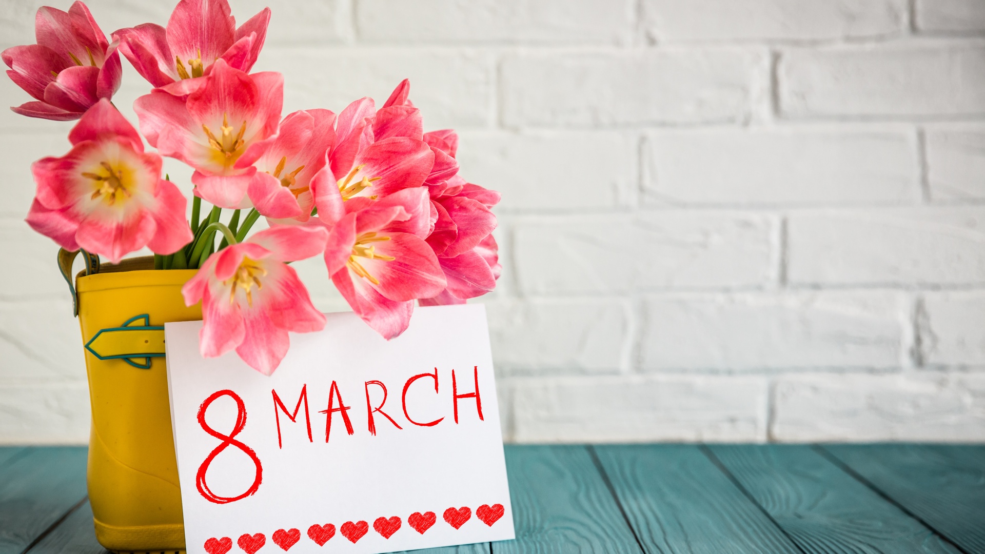粉白郁金香装在亮黄小靴形容器中，旁侧立印有红字的卡片。