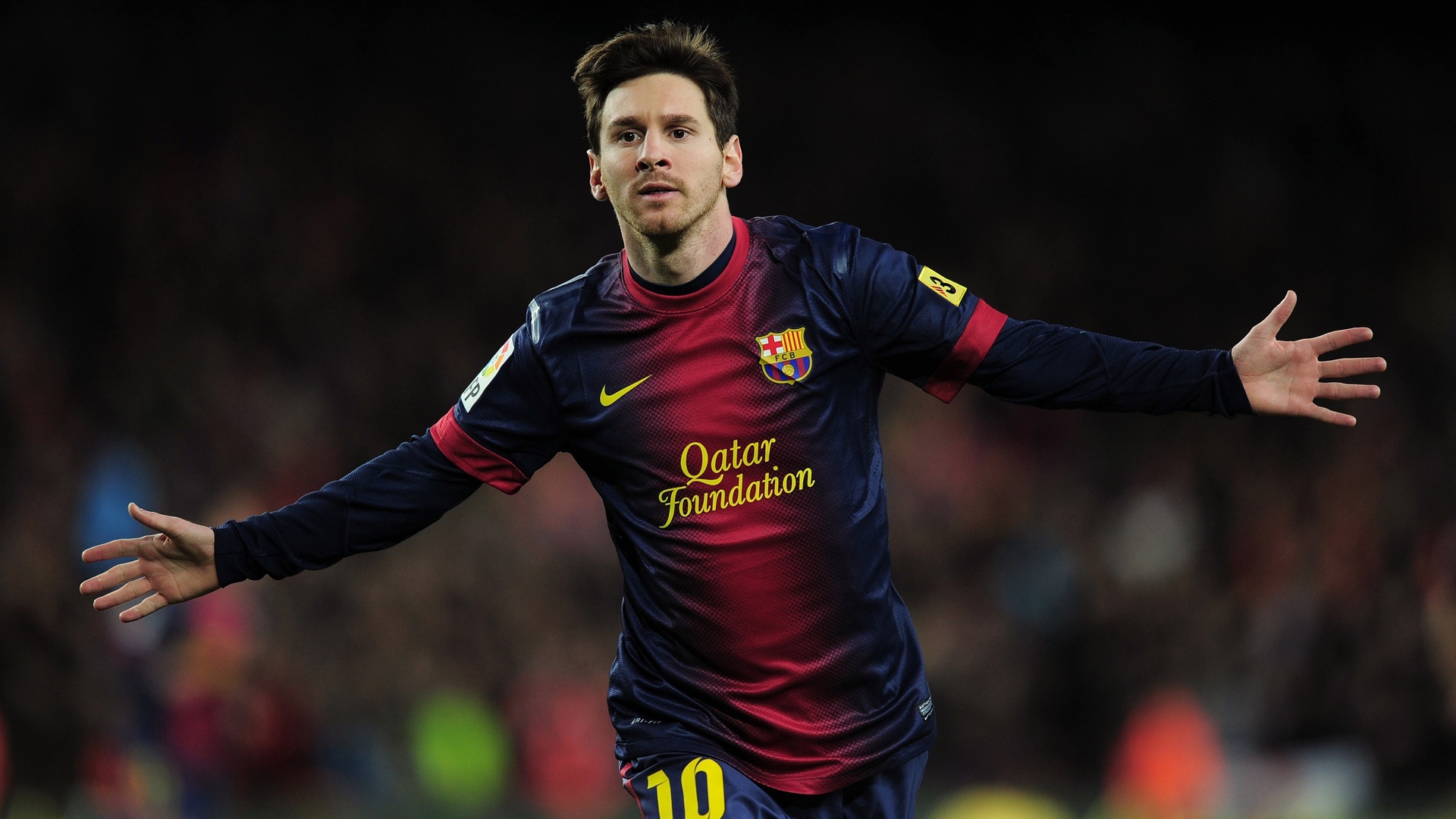 夜间体育场虚化看台前，身着红蓝渐变10号长袖球衣的足球运动员双臂向两侧平展张开。