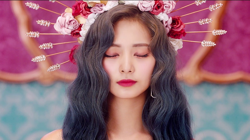 twice主题复古华丽风人像，人物闭着双眼，留深灰黑色长波浪卷发，佩戴花朵放射状头饰与碎钻流苏耳饰，上半为粉紫带金色弧形装饰背景，下半为蓝绿暗纹背景。