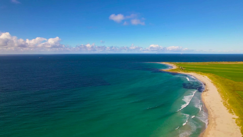 高空航拍弧形海湾，清透绿蓝渐变近海挨着浅金沙滩，旁侧是连片翠绿郊野绿地。