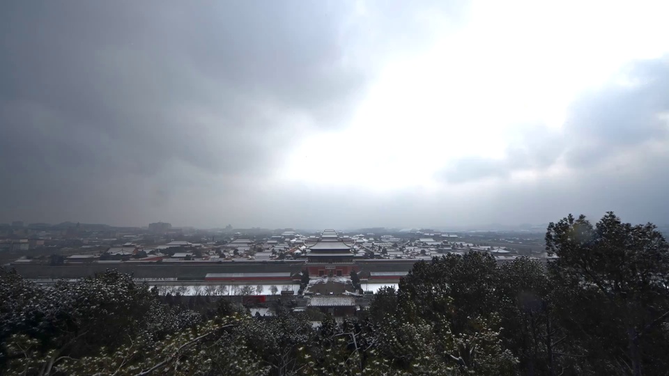 雪景中的覆雪中式皇家宫殿群，前景是积有薄雪的深绿常绿林木，灰调冷色中朱红墙身醒目。