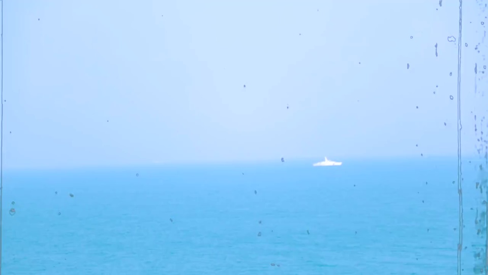 淡蓝色海天一色，远海右侧有一艘白色小船，玻璃上布满细碎污渍。
