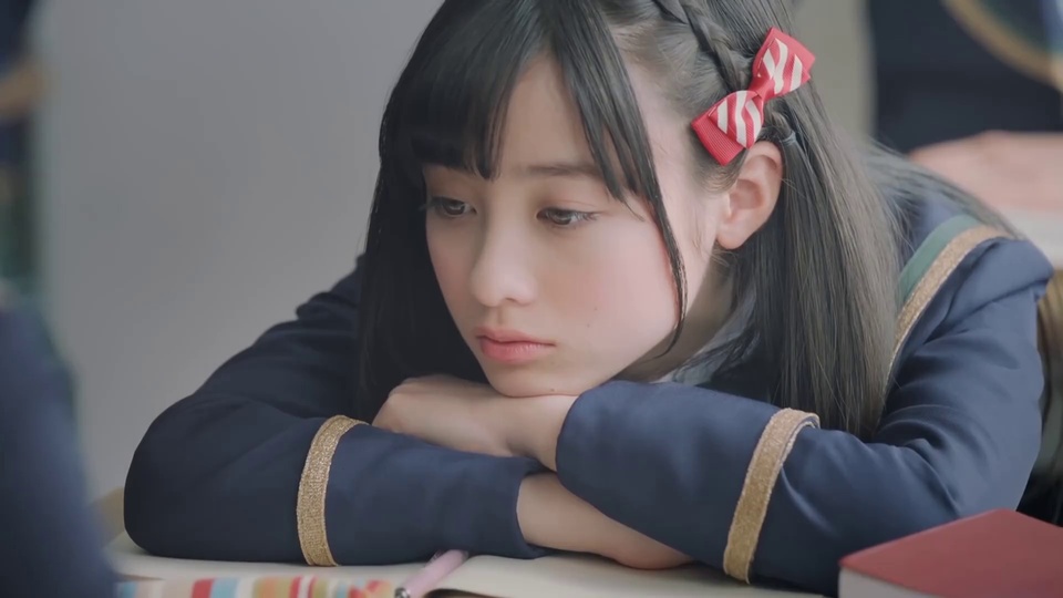 室内教室场景中，身着藏青镶金边长袖制服的长发少女，手肘搭在桌面托腮望向侧方。
