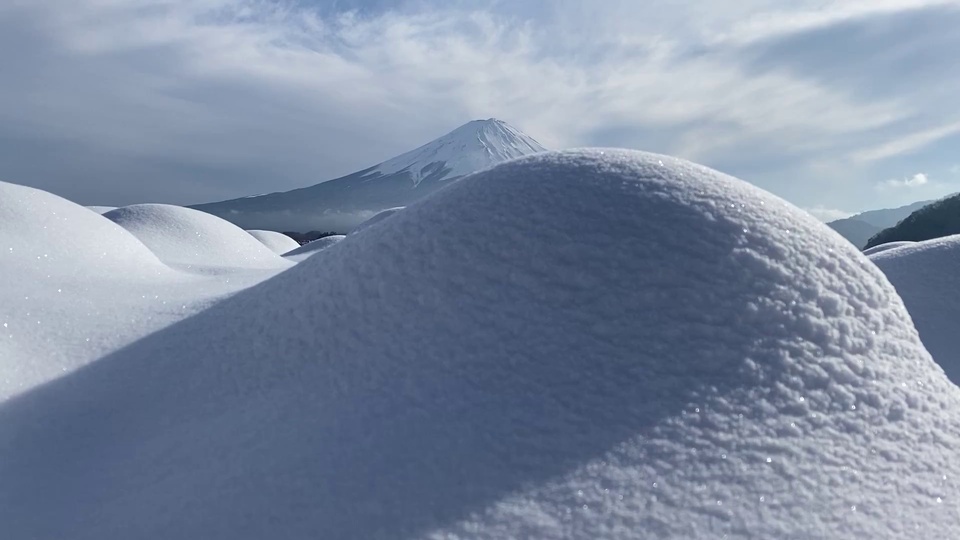前景圆润积雪丘与远景覆雪锥形雪峰，淡蓝天际飘着薄云