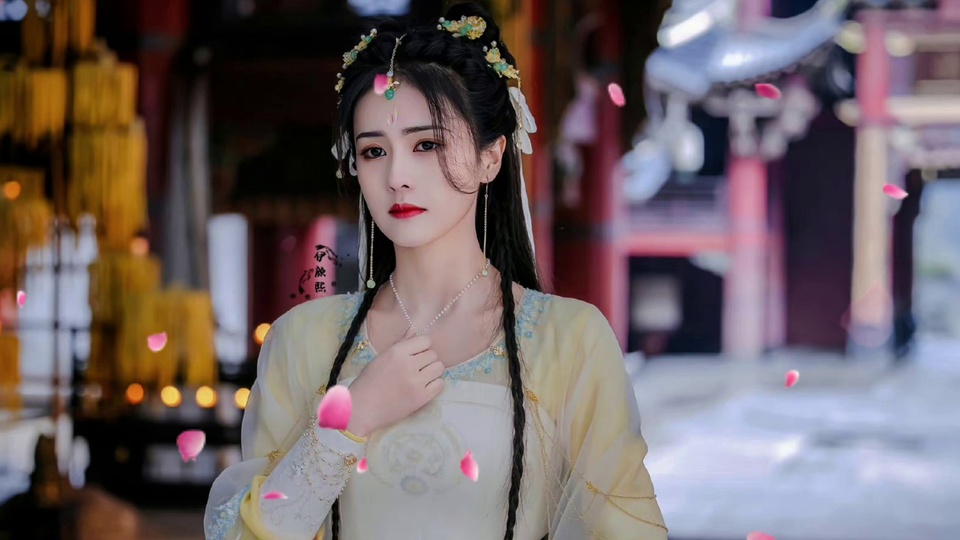 梳古风编发的年轻女性佩戴绿金额饰，身着浅黄白纱衣，右手轻放胸前，背景虚化古建庭院，空中飘满粉色花瓣。