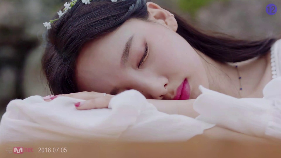 twice主题暖粉调实拍，黑发闭眼少女戴白色小花发饰，手臂垫在脸颊下，配细银链蓝坠项链，红甲带小戒指，背景是虚化户外场景。