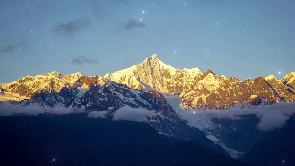 日照金山的覆雪雪山群，蓝天缀星点，山谷云雾缭绕。