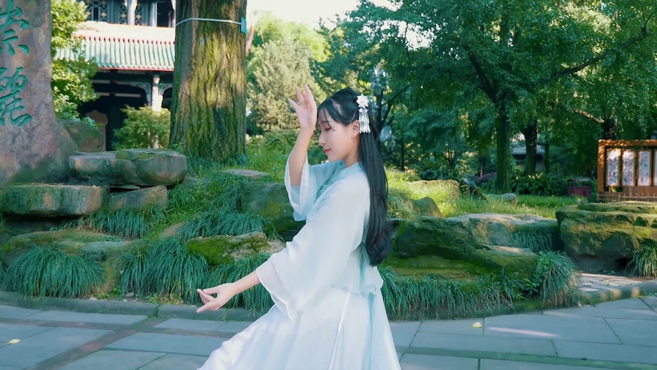 穿浅青色汉服的女子在中式园林石板路上起舞