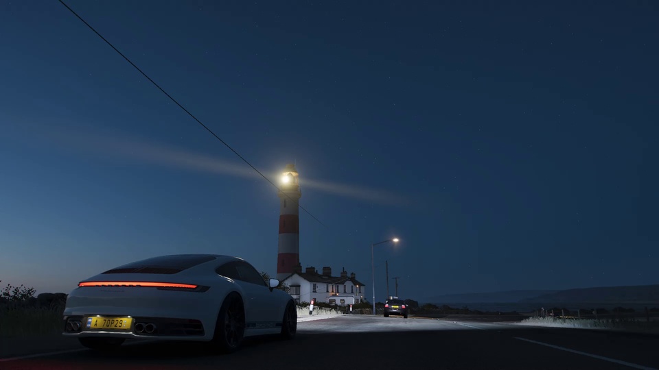 夜间滨海公路上停放白色轿跑，远处是亮灯的红白条纹灯塔