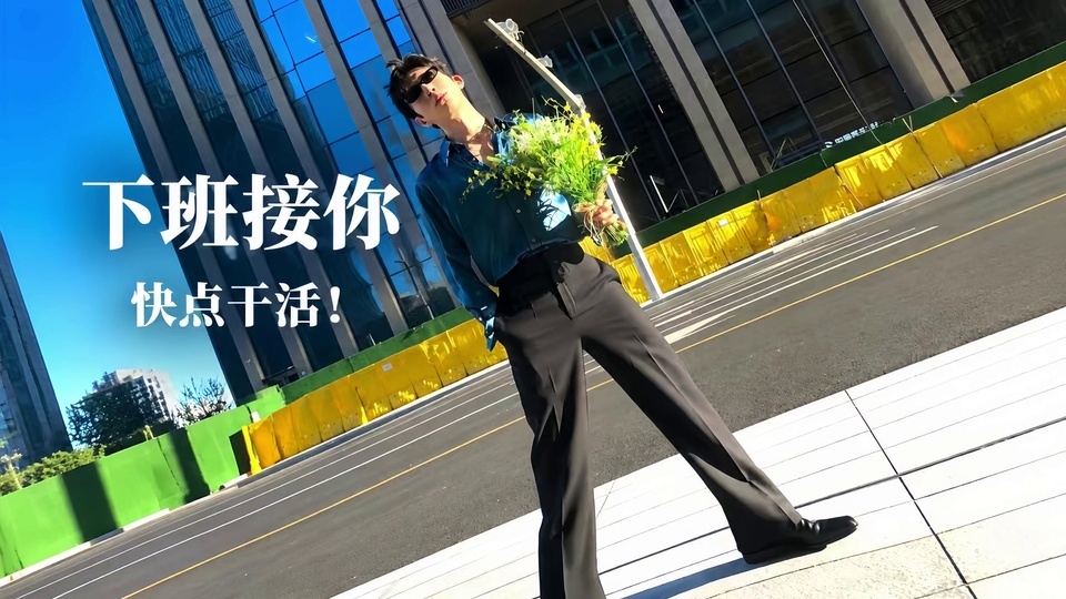 亮蓝色晴空下的城市写字楼街景，戴墨镜的年轻男子穿蓝绿色缎面衬衫、黑色阔腿长裤，手持绿黄色花束单插裤袋站立，画面左侧印有白色文字。