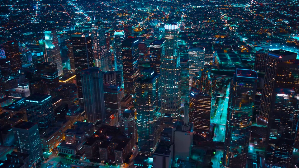 高空航拍视角下的夜晚城市商务区，密集摩天高楼群错落分布，楼体窗灯与轮廓灯交织，呈现青蓝与暖黄灯光搭配深黑夜色的写实夜景画面。