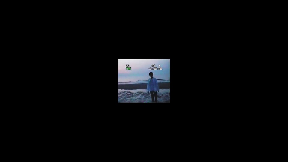 纯黑背景中居中的窄幅tfboys主题复古录像小画面，身着浅色上衣深色长裤的人物站立在沙滩上，带有老式摄像机T30标识与倒计数字样，小画面内呈现淡紫粉渐变天色与浅沙色地面。