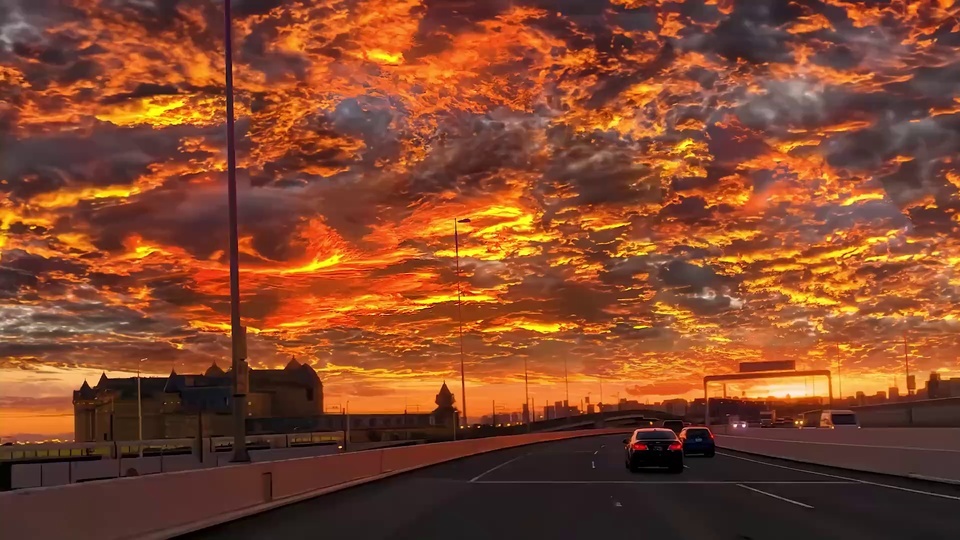 高架道路上行驶的车辆，天空布满橙红与金橙色火烧云。