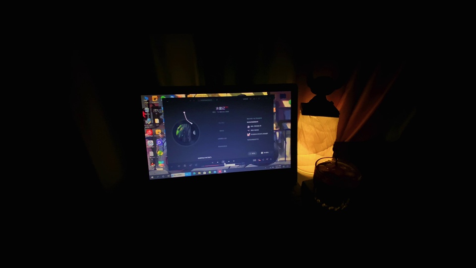 深夜暗光环境中亮屏的笔记本电脑，旁侧立着散发暖光的桌面灯，近侧放置深色玻璃杯