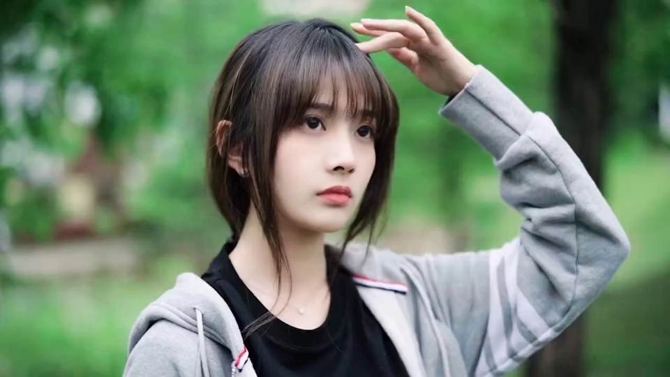 穿灰色连帽外套的少女在绿意虚化的户外抬起左手