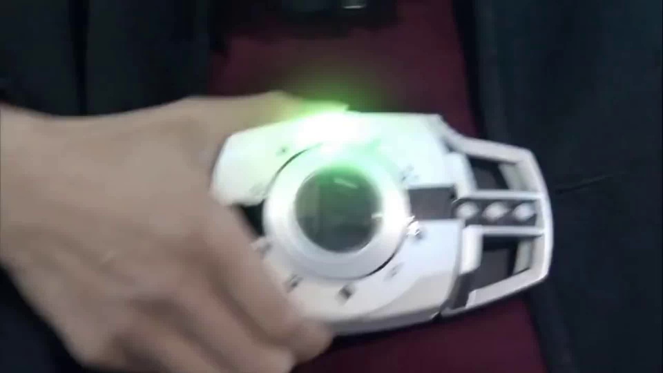 特写画面中浅色的手正在触碰银白机械装置，装置中心发出刺眼的绿色亮光。