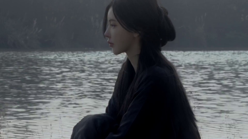 黑衣长发女子侧坐湖畔，面朝灰蒙水面望向远方