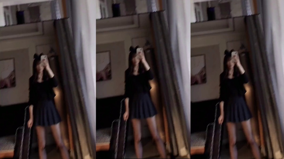室内镜前自拍场景，戴黑色蝴蝶结的黑丝美女身着黑色长袖上衣、黑色百褶短裙与黑色丝袜，手持手机对镜自拍，背景墙面有装饰画与长窗帘。