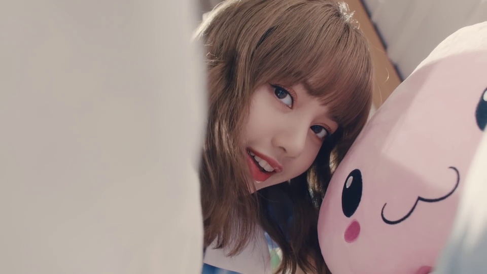 Lisa blackpink主题暖调室内近景人像，浅棕色齐刘海中长发年轻女性身旁摆放粉色卡通毛绒公仔，左侧有模糊浅色遮挡物。