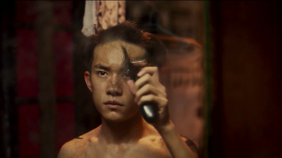 昏暗暖红暗棕调的室内，一名赤裸上身的年轻男性手持黑色电动理发推子，背景模糊，采用复古写实风格。