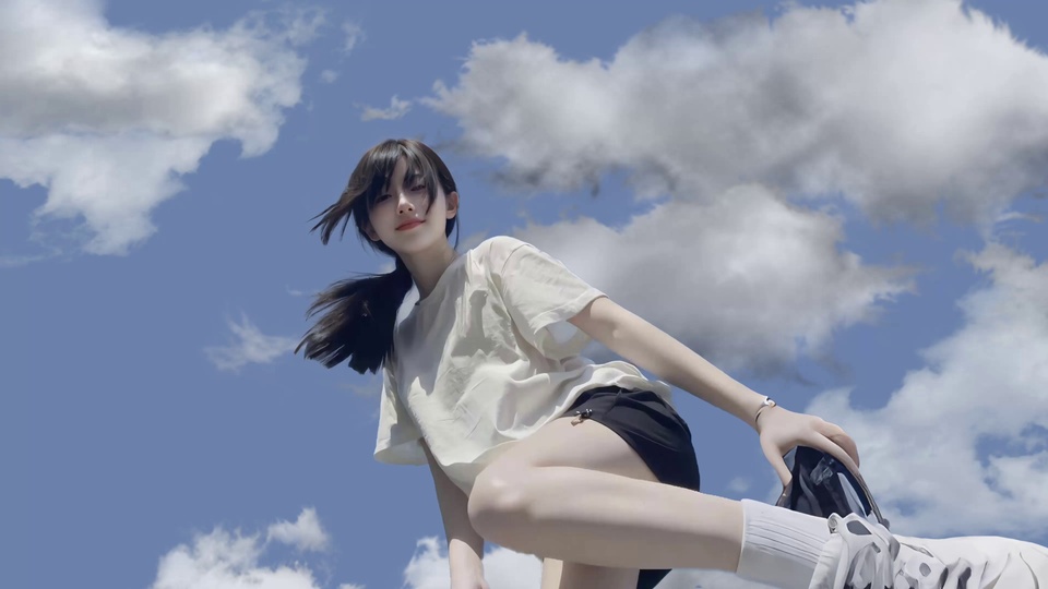 低角度仰视身着白短袖黑短裤的女孩立于蓝白云层前