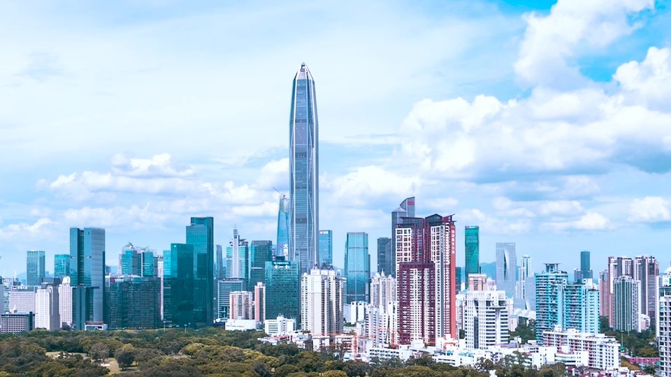 蓝天白云下的现代城市摩天楼群天际线，前景覆盖连片茂密绿树。