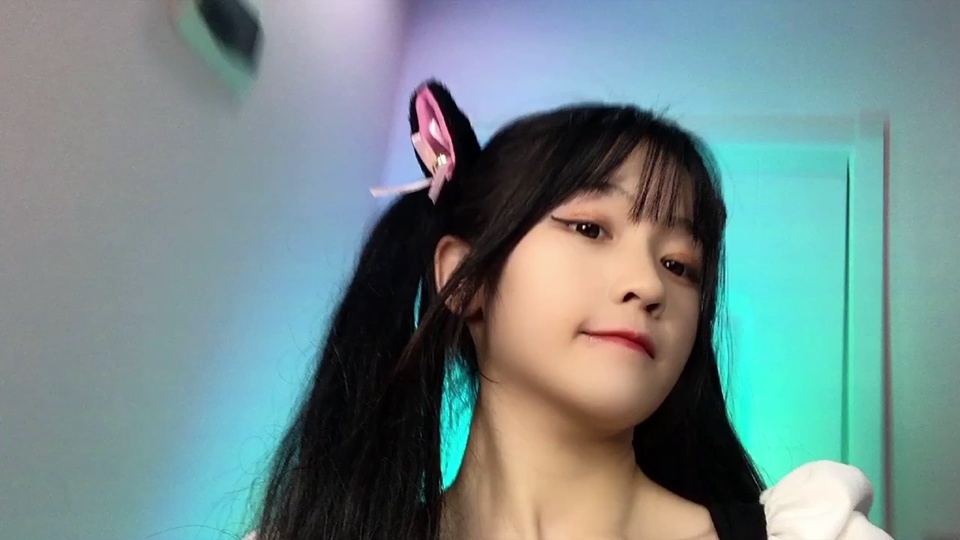佩戴粉色发饰的双马尾黑发少女近景，背景是青蓝色虚化室内墙面