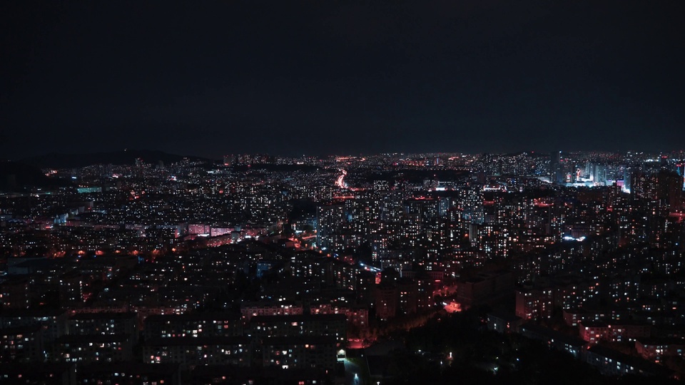 高空俯瞰的连片城市夜景，暗黑夜空下遍布暖红与冷白色的城市灯火