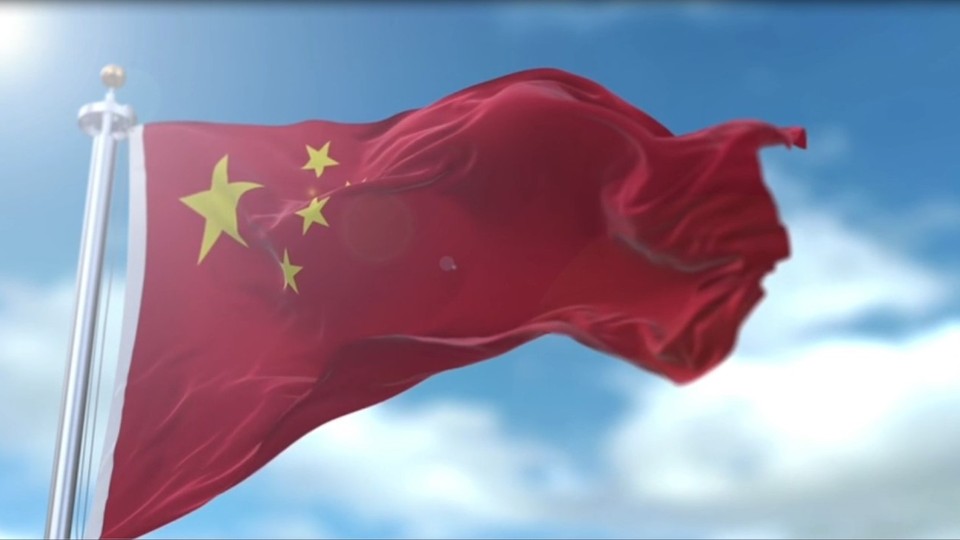 蔚蓝色天空点缀着轻薄白云，阳光散发光晕，银色旗杆上正红色的五星红旗迎风舒展。