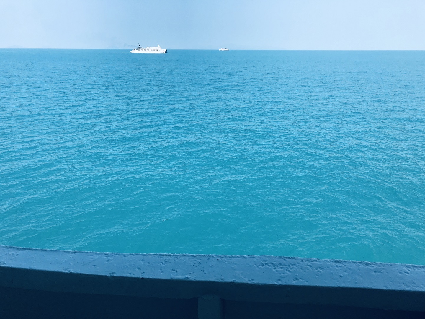 澄澈蓝绿色开阔海面与浅蓝晴空相接，远处海面分布两艘白色船只，整体色调清新明净。