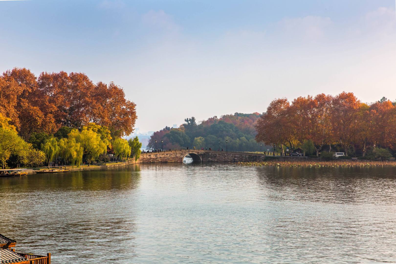 秋日湖畔石拱桥与两岸橙红林木的郊野风景