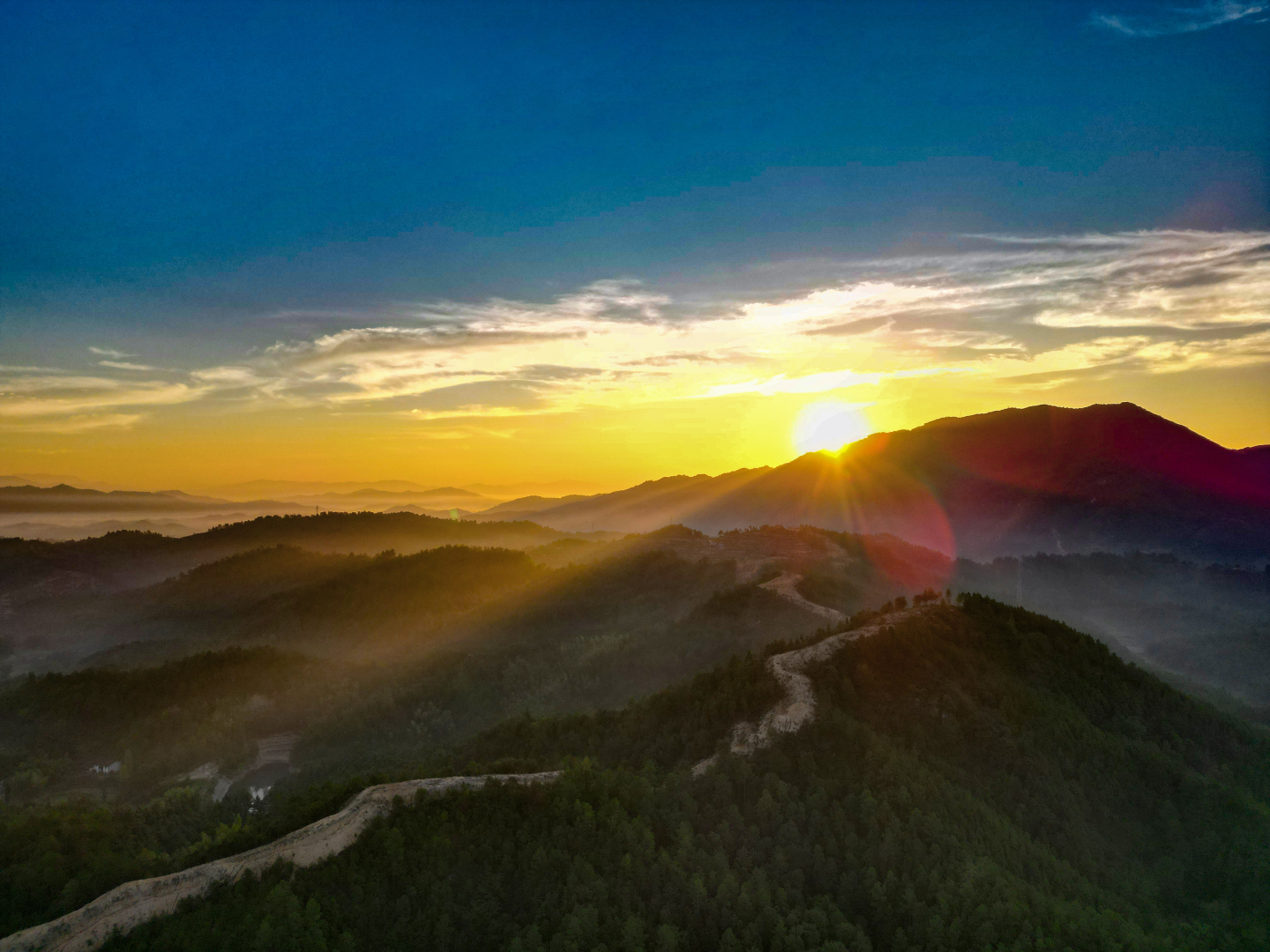 日出时分，金色阳光洒向层叠山林，薄雾缭绕，山脊土路蜿蜒向前。