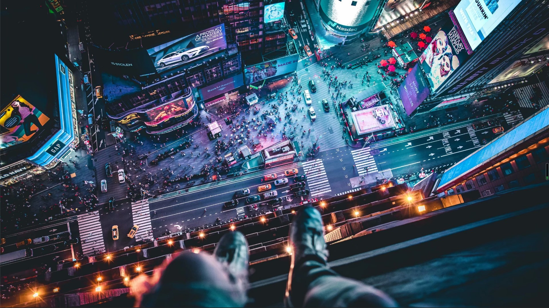 高空俯瞰霓虹交织的繁华城市夜景，前景可见垂落的裤腿与鞋尖。