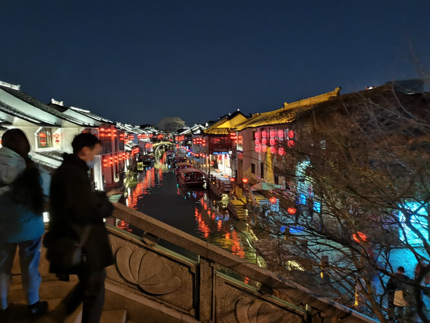 入夜的水乡古街，河道两岸白墙黑瓦古建挂满红灯笼，河面映着灯火倒影。