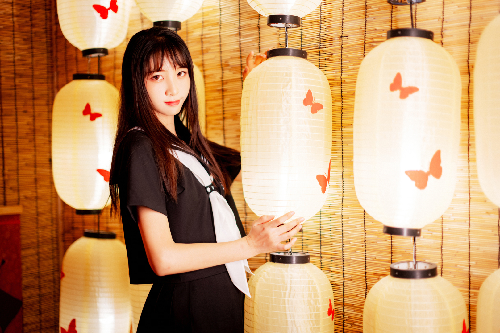 黑发少女扶着印红色蝴蝶纹样的暖光纸灯笼站在竹帘前