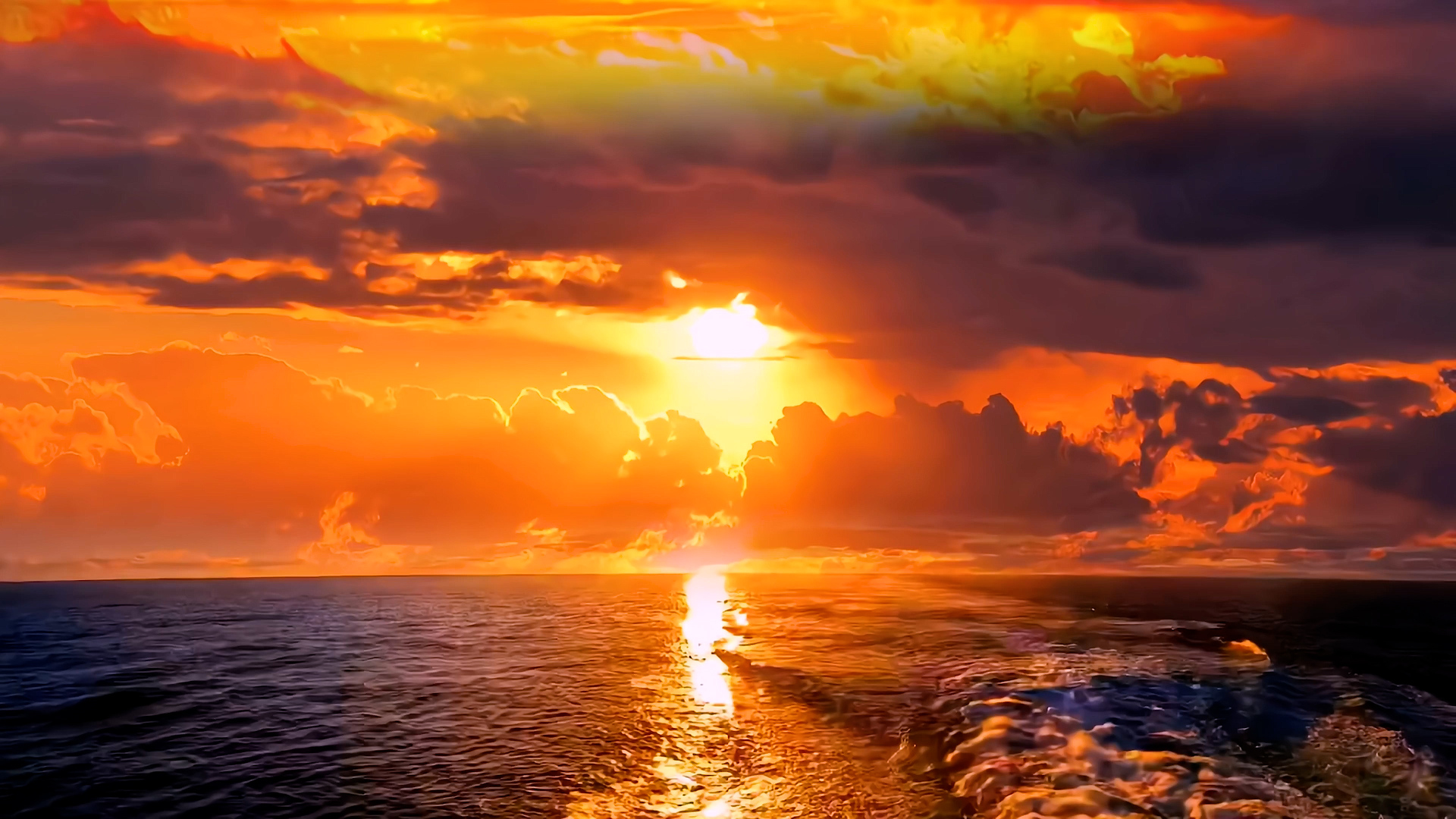 海平面落日海景，暖黄色太阳低悬于海面，海面中央延伸出明亮的阳光反射带，天空被橙红、明黄与深紫的霞光照亮，海面呈深暗蓝黑色。