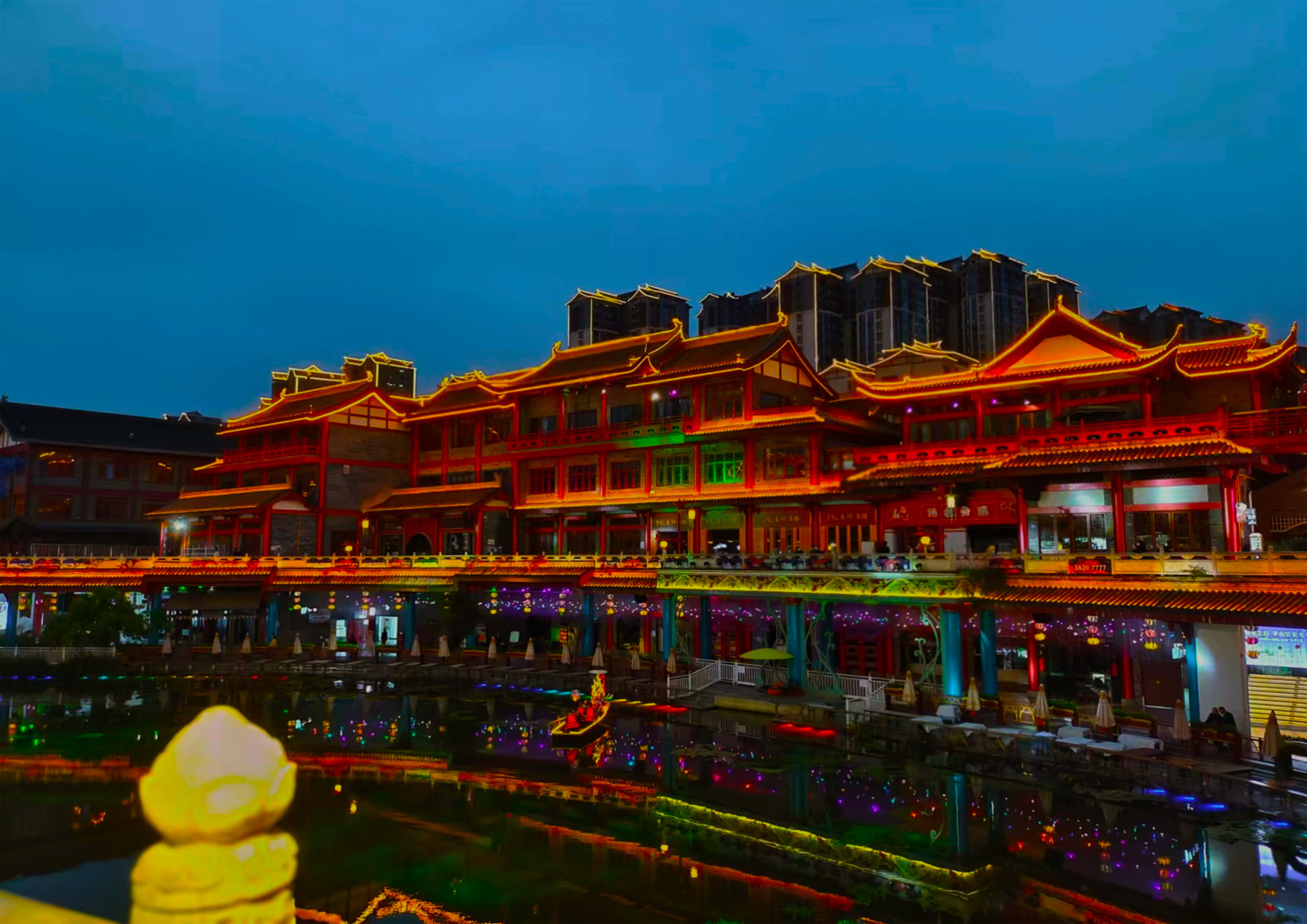 夜色里被霓虹点亮的临水中式古建，灯光完整倒映在平静水面上