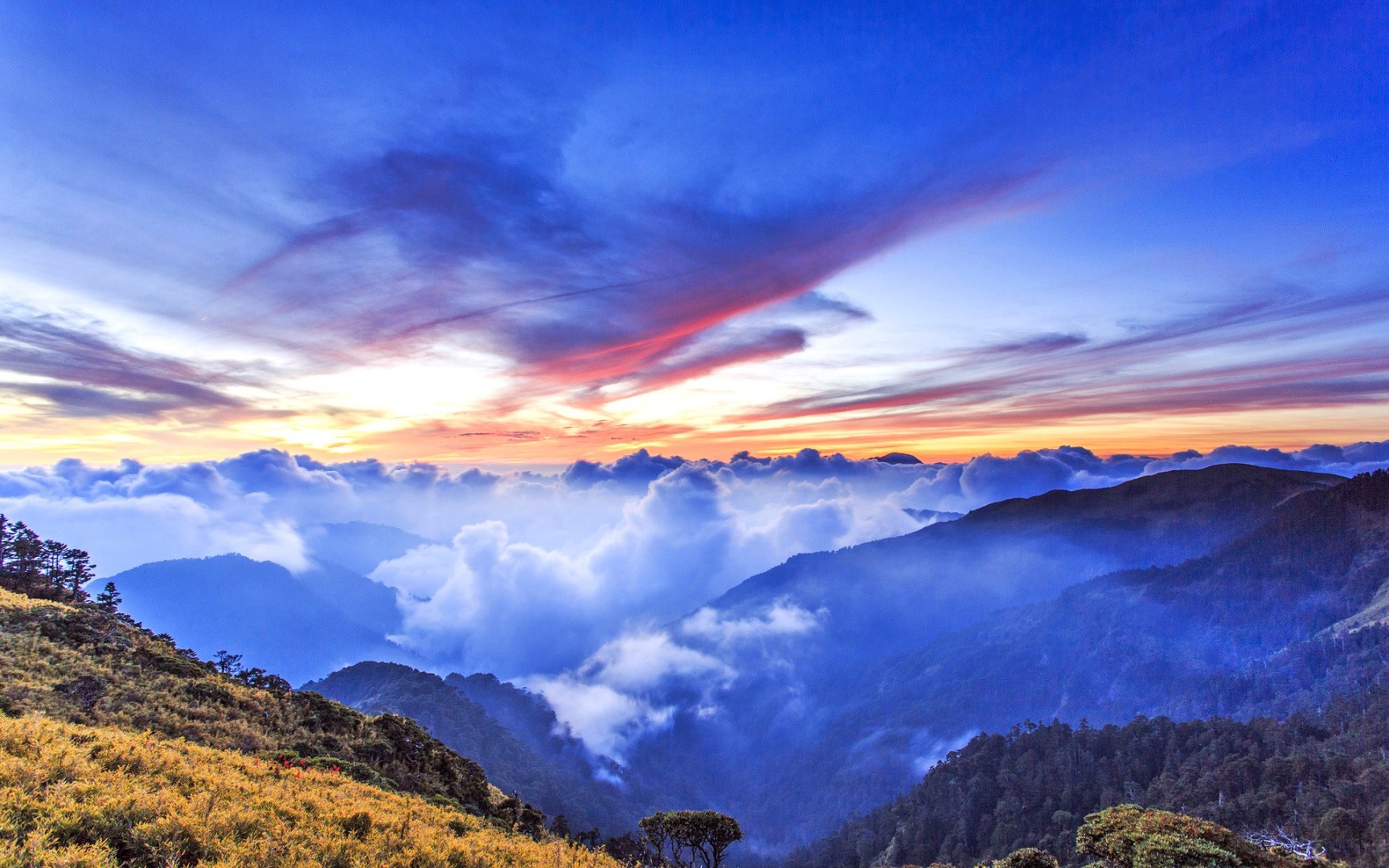 高海拔山地上空的朝霞云海，层叠青山在云海间露出，条带状云团晕染着暖金与粉紫色调